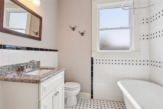 bathroom featuring a washtub, tile patterned floors, toilet, vanity, and tile walls