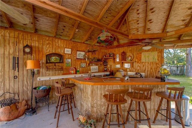 bar with vaulted ceiling, ceiling fan, and wooden walls