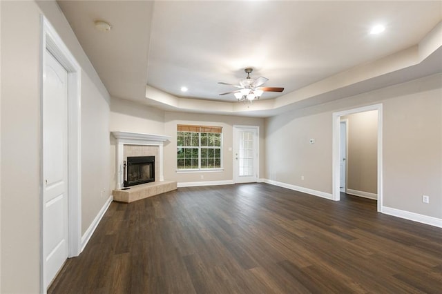 unfurnished living room with a raised ceiling, a tiled fireplace, ceiling fan, and dark wood-type flooring