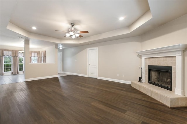 unfurnished living room with ceiling fan, a raised ceiling, dark wood-type flooring, and a tile fireplace