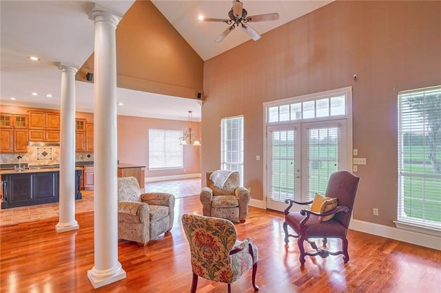 living room with a wealth of natural light, ceiling fan with notable chandelier, high vaulted ceiling, and light hardwood / wood-style flooring