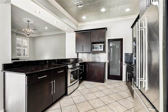 kitchen with appliances with stainless steel finishes, dark stone counters, dark brown cabinetry, light tile patterned floors, and a notable chandelier