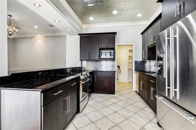 kitchen featuring dark stone counters, stainless steel appliances, crown molding, light tile patterned floors, and a chandelier