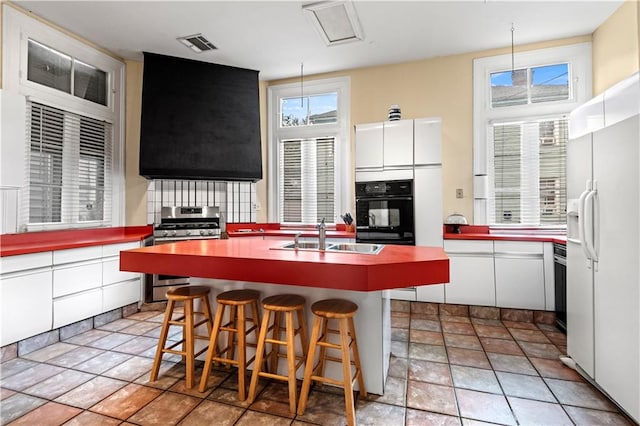 kitchen featuring gas range, white cabinetry, sink, white refrigerator with ice dispenser, and black oven