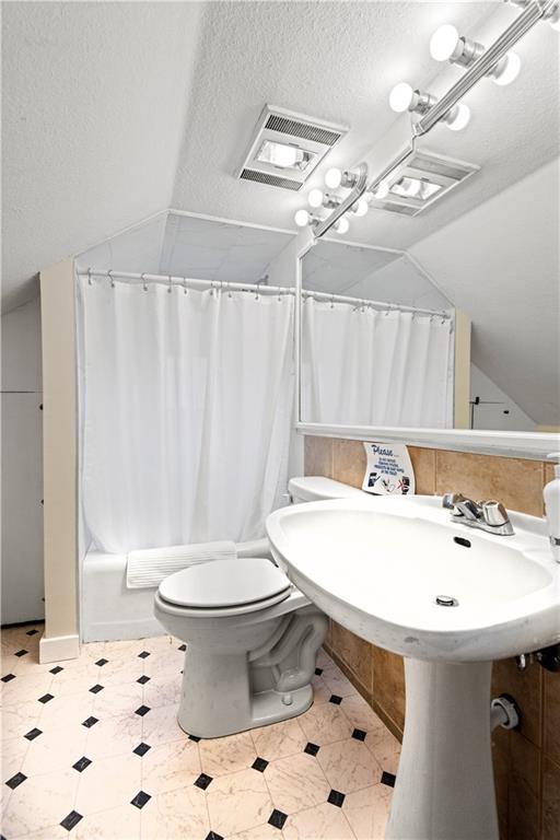 bathroom featuring toilet, lofted ceiling, a textured ceiling, and shower / tub combo with curtain