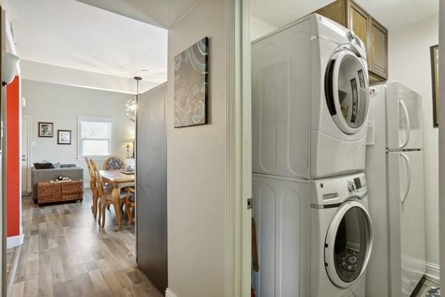 washroom featuring stacked washer / dryer, cabinets, and light wood-type flooring