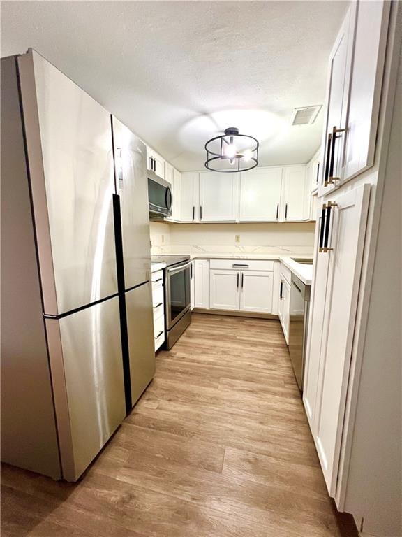 kitchen with appliances with stainless steel finishes, a textured ceiling, light hardwood / wood-style flooring, and white cabinetry