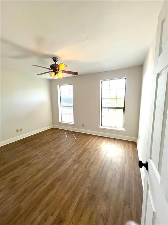 spare room featuring dark wood-type flooring, ceiling fan, and a healthy amount of sunlight