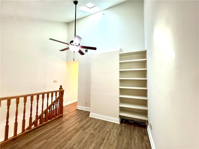 interior space featuring hardwood / wood-style flooring, ceiling fan, a towering ceiling, and a skylight