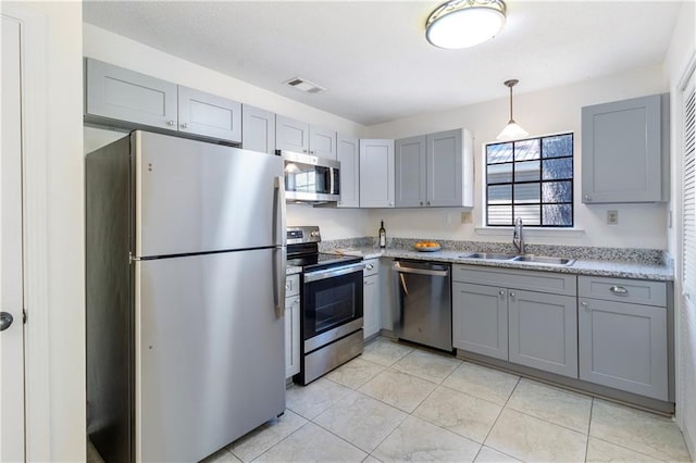 kitchen with gray cabinetry, sink, hanging light fixtures, light stone counters, and stainless steel appliances