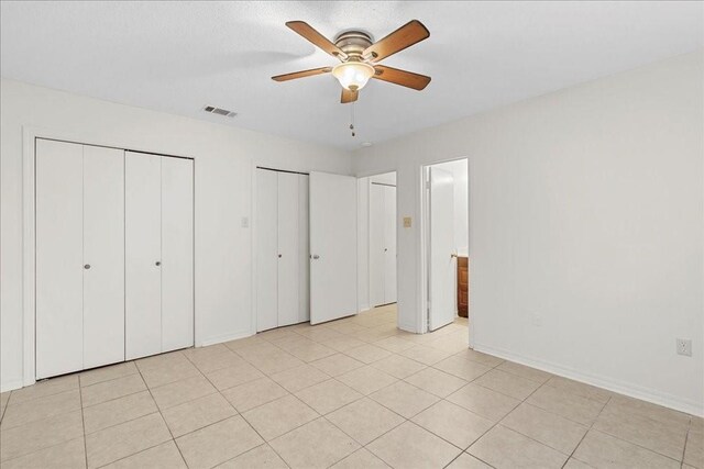 unfurnished bedroom with ceiling fan, light tile patterned floors, and two closets