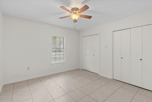 unfurnished bedroom with light tile patterned floors, ceiling fan, and multiple closets