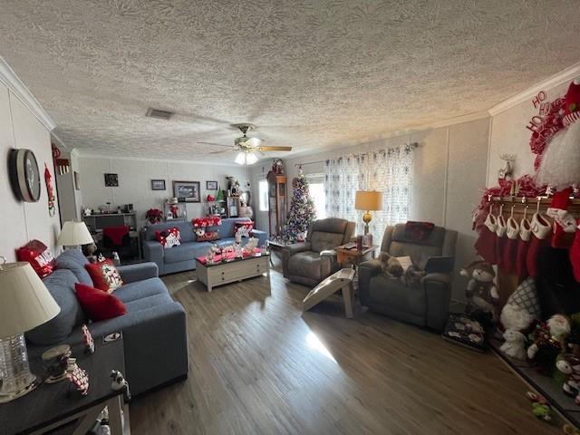 living room featuring a textured ceiling, wood finished floors, visible vents, a ceiling fan, and crown molding