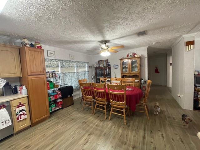 dining room featuring light wood finished floors, ceiling fan, visible vents, and a textured ceiling