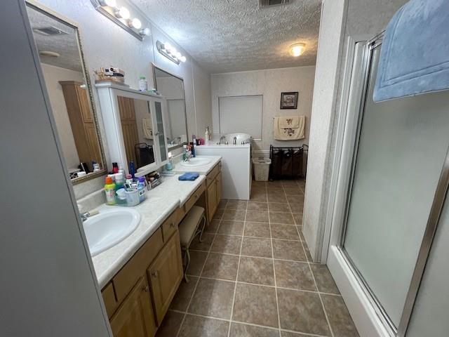 full bath with a sink, a shower with door, tile patterned flooring, and a textured ceiling