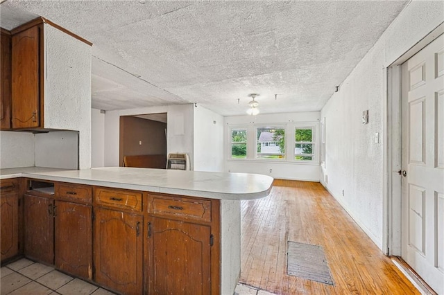 kitchen with heating unit, kitchen peninsula, a textured ceiling, and light hardwood / wood-style flooring