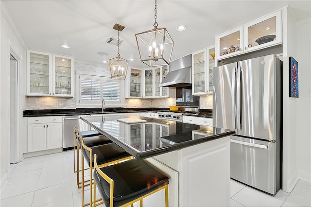 kitchen featuring appliances with stainless steel finishes, a breakfast bar, wall chimney range hood, pendant lighting, and a kitchen island