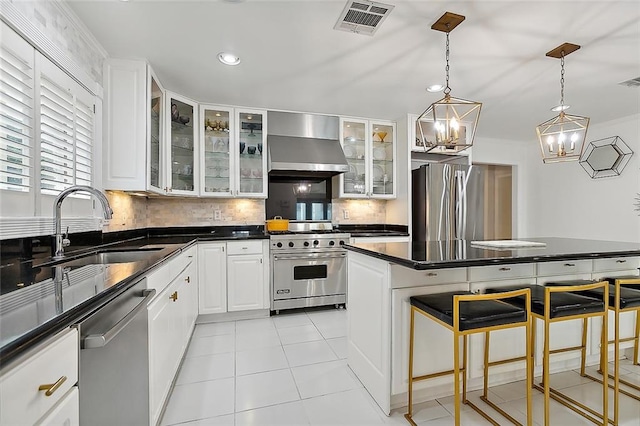 kitchen featuring appliances with stainless steel finishes, backsplash, wall chimney range hood, decorative light fixtures, and white cabinets