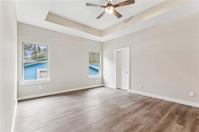 spare room with hardwood / wood-style floors, ceiling fan, a wealth of natural light, and a raised ceiling