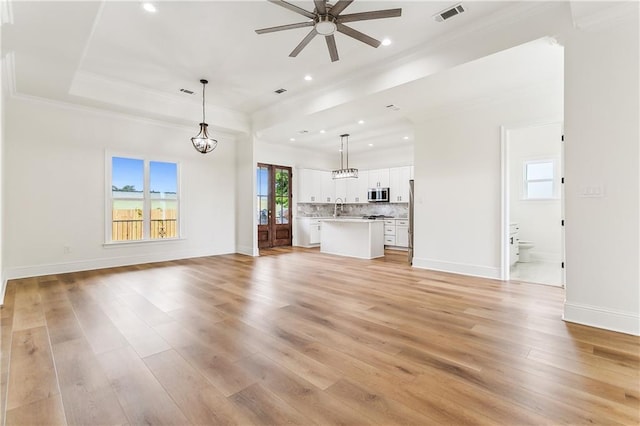 unfurnished living room featuring sink, crown molding, light hardwood / wood-style flooring, ceiling fan, and a tray ceiling