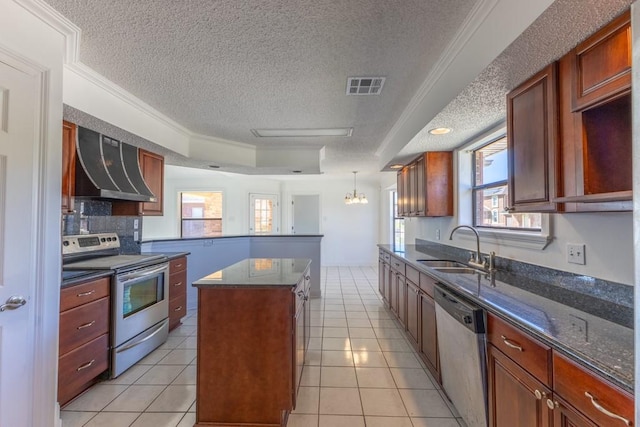 kitchen with sink, wall chimney exhaust hood, stainless steel appliances, a textured ceiling, and a kitchen island