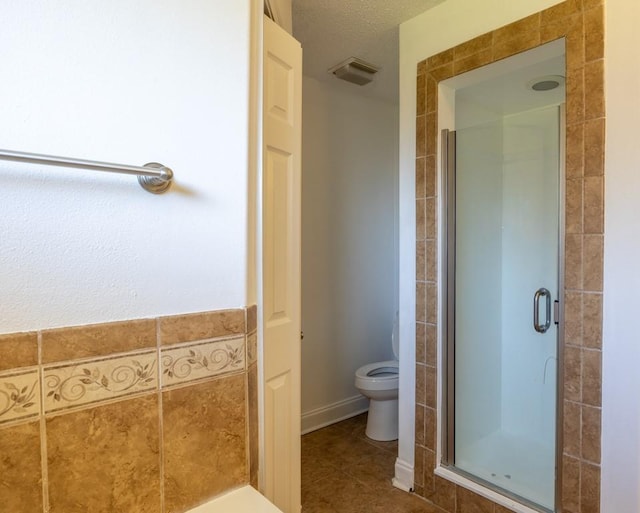 bathroom featuring a textured ceiling, tile walls, tile patterned flooring, toilet, and a shower with shower door