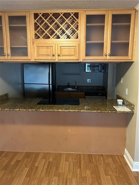 kitchen featuring black appliances, stone counters, sink, and hardwood / wood-style flooring