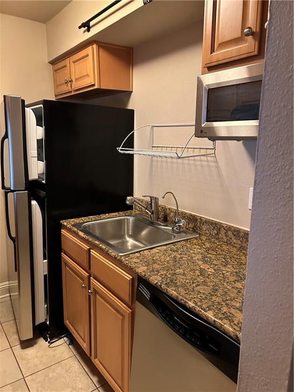 kitchen with light tile patterned floors, stainless steel appliances, dark stone countertops, and sink