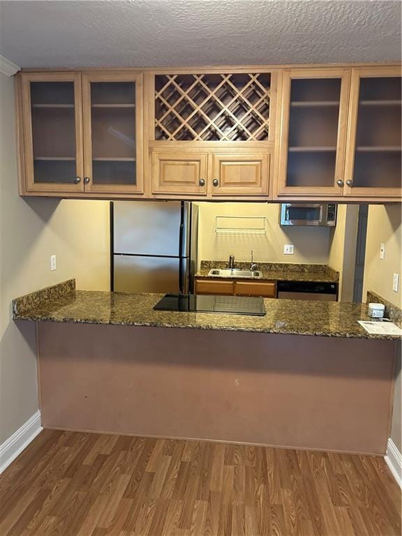 kitchen with sink, dark stone countertops, dark hardwood / wood-style flooring, kitchen peninsula, and stainless steel appliances