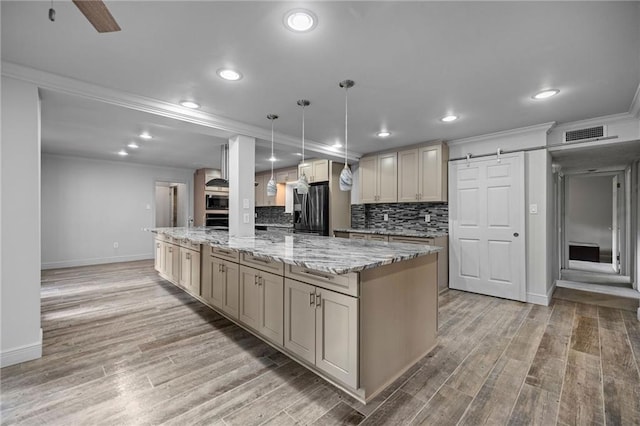 kitchen with light hardwood / wood-style flooring, a barn door, decorative light fixtures, light stone counters, and stainless steel appliances