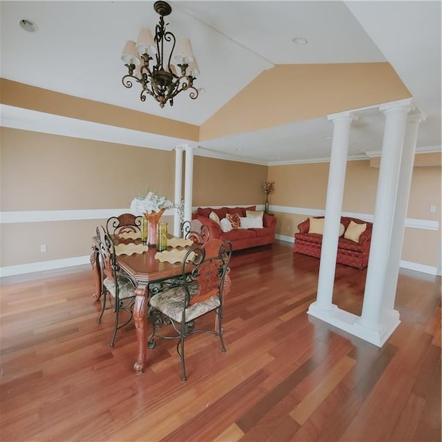 dining space with a notable chandelier, decorative columns, crown molding, vaulted ceiling, and hardwood / wood-style flooring