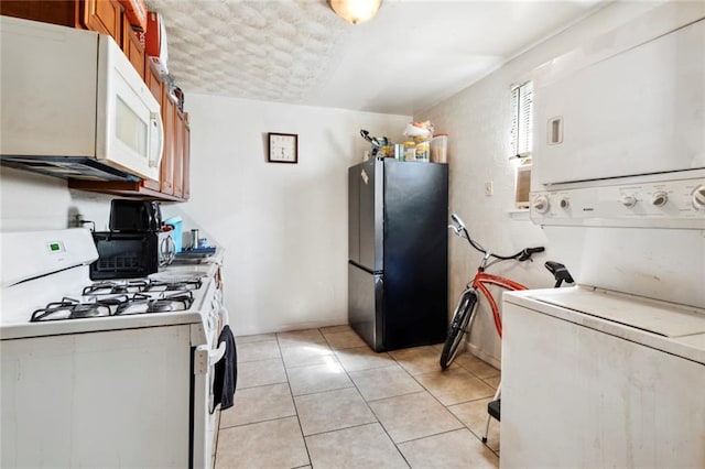 kitchen featuring light tile patterned flooring, white appliances, and stacked washer and clothes dryer