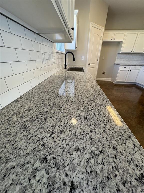 kitchen featuring light stone countertops, decorative backsplash, white cabinetry, and sink