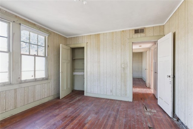 unfurnished bedroom featuring dark hardwood / wood-style flooring, wooden walls, and multiple windows