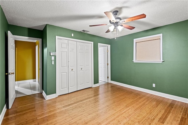 unfurnished bedroom with ceiling fan, a closet, a textured ceiling, and light hardwood / wood-style flooring