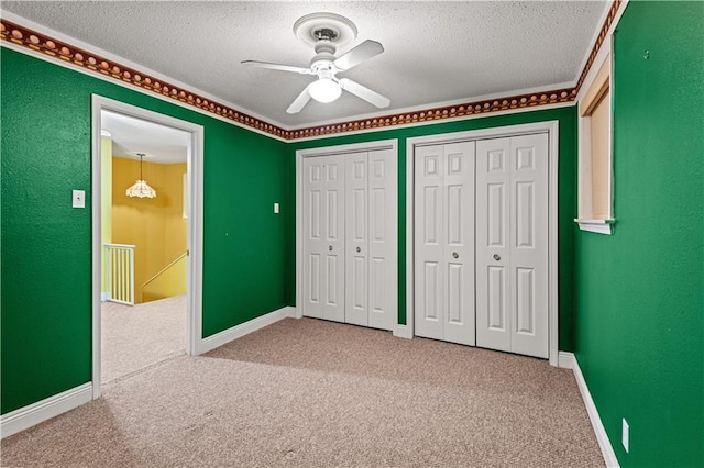 unfurnished bedroom featuring carpet, a textured ceiling, ceiling fan, and multiple closets