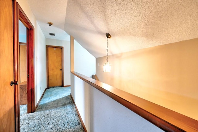 hall with carpet flooring, a textured ceiling, and vaulted ceiling