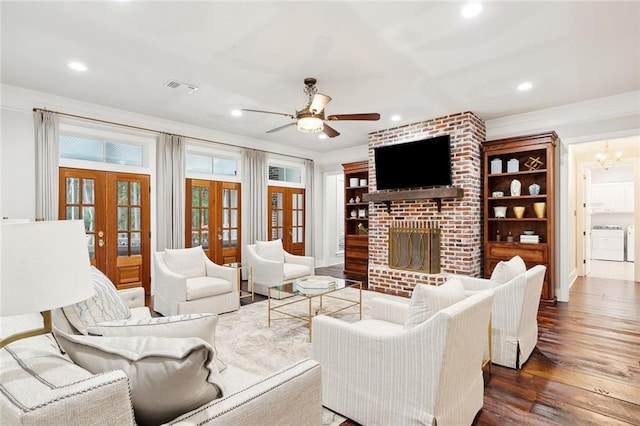 living room with french doors, a brick fireplace, ceiling fan with notable chandelier, washer and dryer, and dark hardwood / wood-style floors