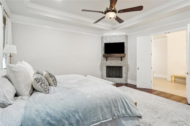 bedroom featuring a tray ceiling, ceiling fan, crown molding, a fireplace, and hardwood / wood-style floors