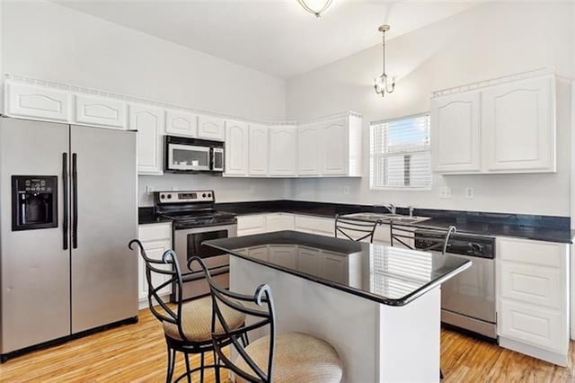 kitchen featuring appliances with stainless steel finishes, light wood-type flooring, vaulted ceiling, sink, and hanging light fixtures