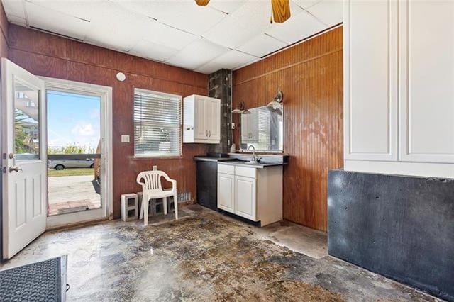 kitchen featuring ceiling fan, wood walls, concrete flooring, and white cabinetry