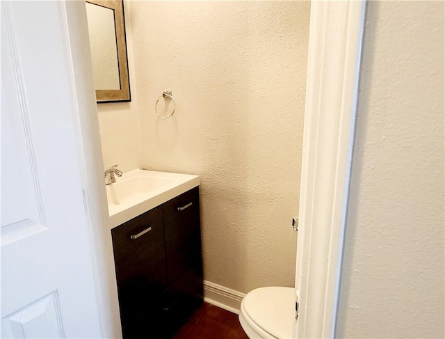 half bath featuring toilet, baseboards, and vanity