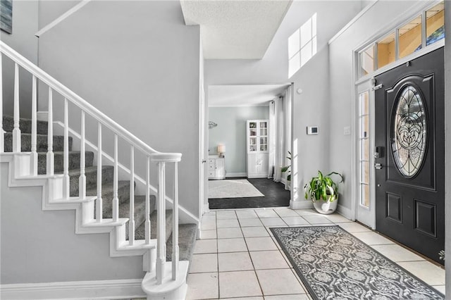 foyer entrance featuring a healthy amount of sunlight, tile patterned floors, stairway, and a textured ceiling