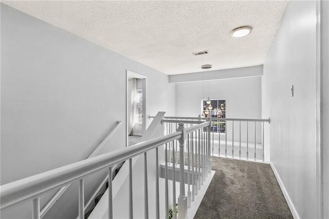 hallway featuring carpet flooring, a textured ceiling, an upstairs landing, visible vents, and baseboards