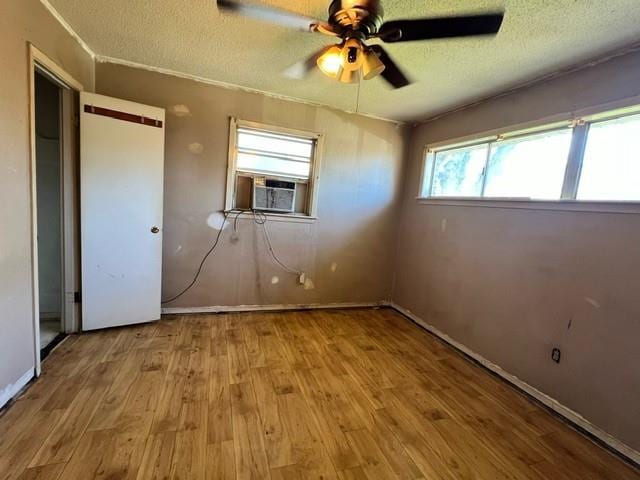 unfurnished bedroom featuring ceiling fan, cooling unit, light hardwood / wood-style floors, and a textured ceiling