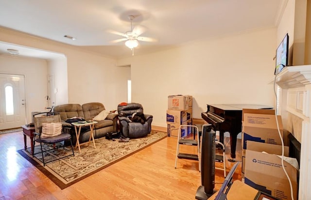 living room with hardwood / wood-style floors, ceiling fan, ornamental molding, and a tiled fireplace