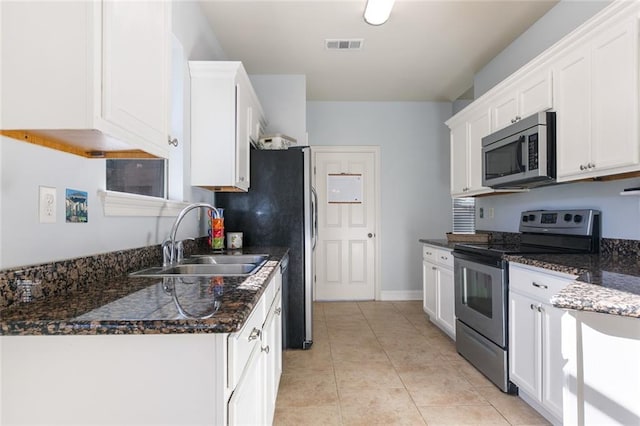 kitchen with sink, light tile patterned flooring, dark stone countertops, white cabinets, and appliances with stainless steel finishes