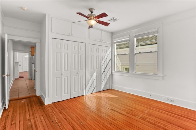 unfurnished bedroom featuring multiple closets, ceiling fan, and light hardwood / wood-style floors