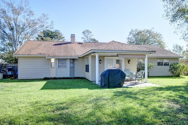 rear view of house featuring a patio area, roof with shingles, a chimney, and a yard