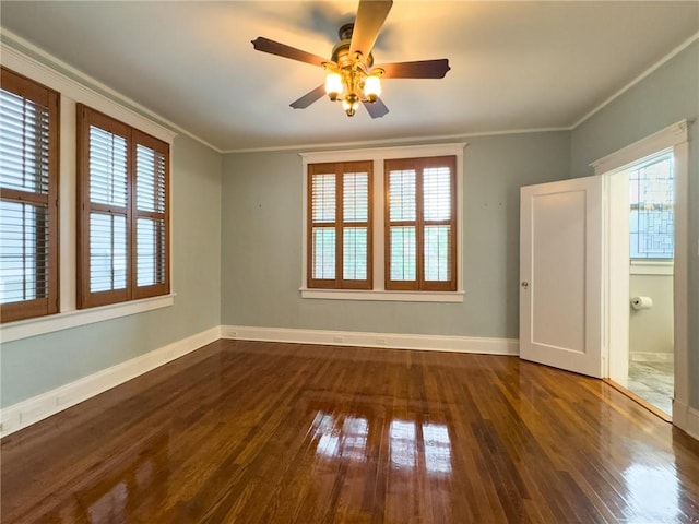 empty room featuring ornamental molding, dark wood-type flooring, ceiling fan, and a healthy amount of sunlight